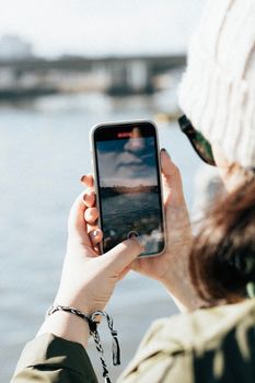 Woman filming scenic water view using smartphone outdoors.