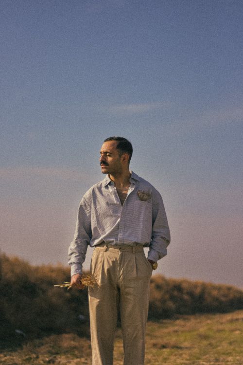 Free A man wearing beige trousers and a shirt standing in a field holding straw, evoking a serene summer landscape. Stock Photo