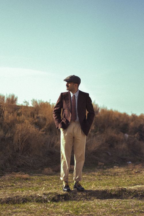 Free Man in vintage attire poses in a grassy outdoor setting. Stock Photo