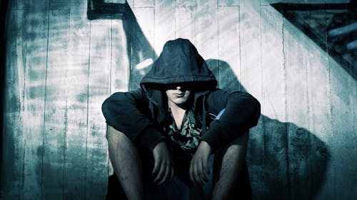 Person Wearing Black Zip Hoodie Sitting in Front of Gray Wooden Plank Wall during Nighttime