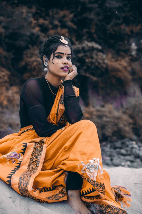 Free A graceful Indian woman in a vibrant orange saree poses outdoors, showcasing traditional attire. Stock Photo