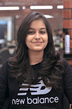 Young woman with brunette hair smiling in a salon wearing a fashionable sweatshirt.
