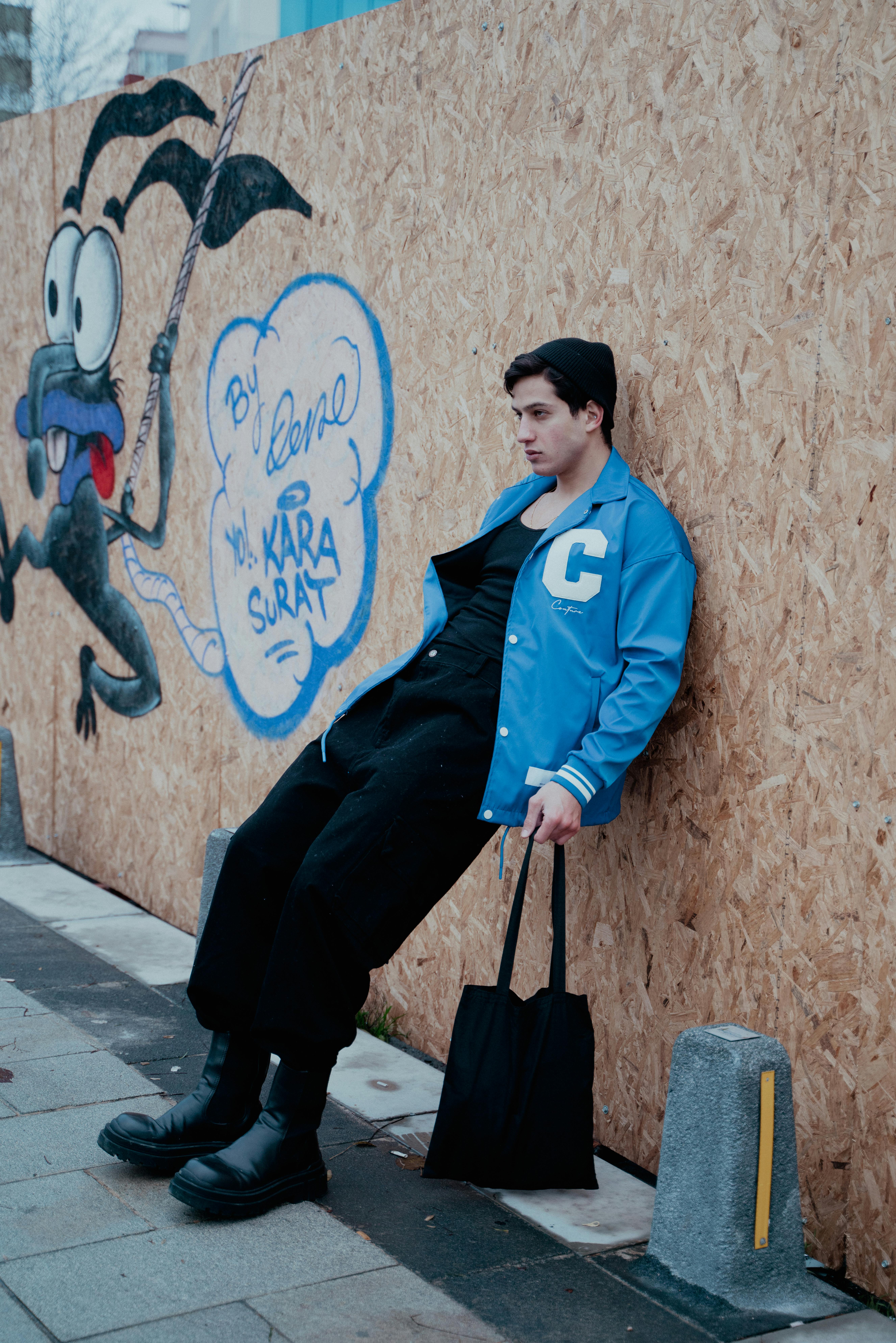 Young man in street fashion leaning against a graffiti wall in İstanbul.