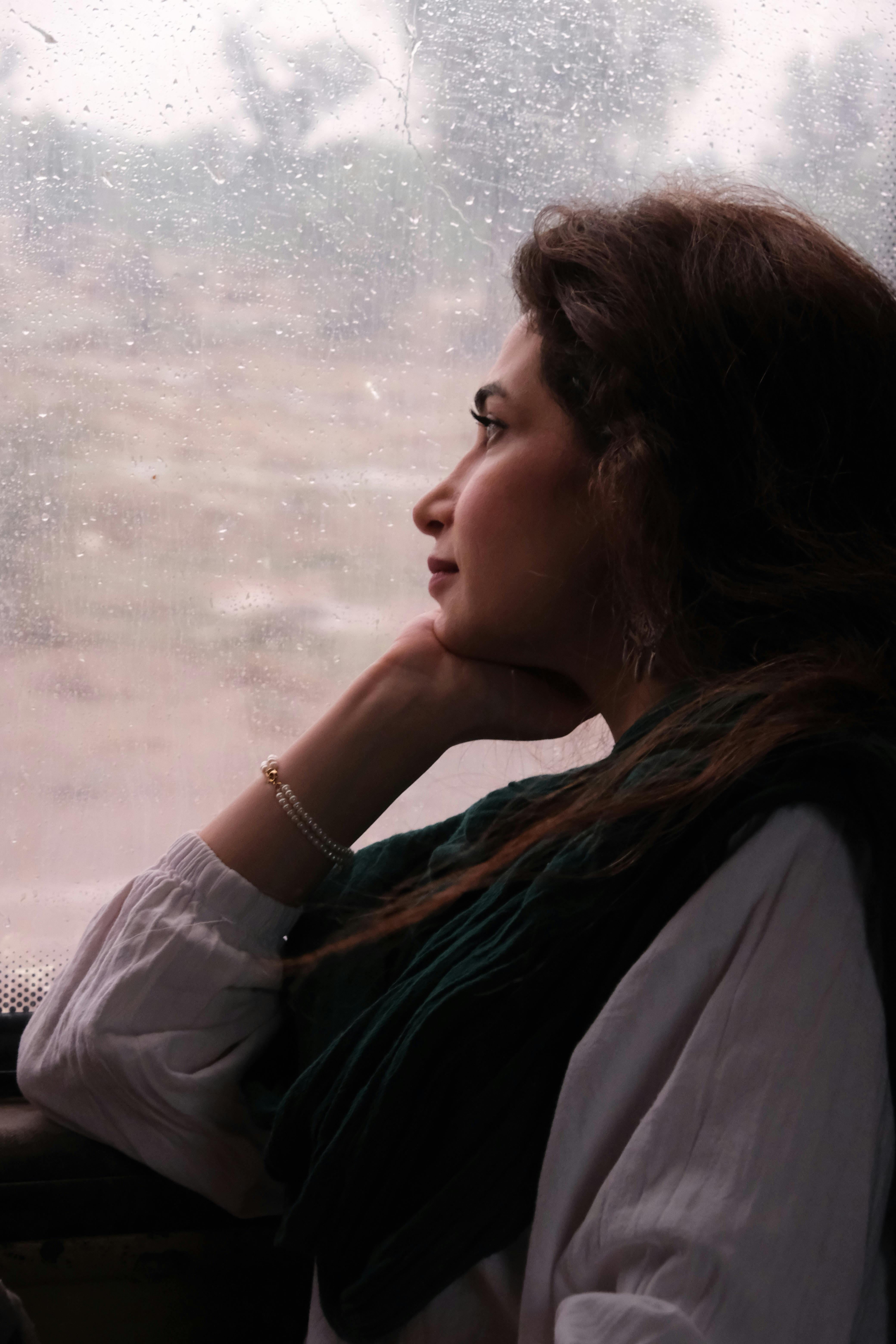 A woman in thoughtful contemplation as she gazes out a rainy train window, capturing the mood of travel.