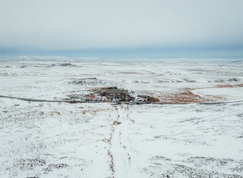 Drone view of a snowy landscape featuring a remote pub surrounded by vast snow-covered fields.