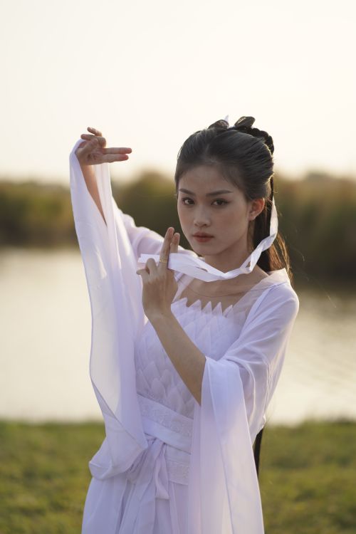 Free Asian woman in traditional attire posing gracefully by a serene lakeside setting. Stock Photo