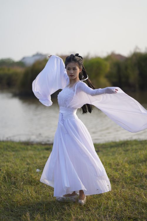 Free A woman dances gracefully in a flowing white dress by the water outdoors. Stock Photo