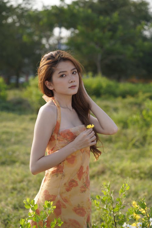 Young Woman in a Dress Standing on a Grass Field 