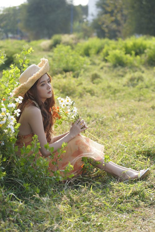 Young Woman Sitting on a Grass Field and Holding Flowers