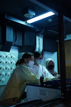 Three women working in a dimly lit laboratory, focused on a project.