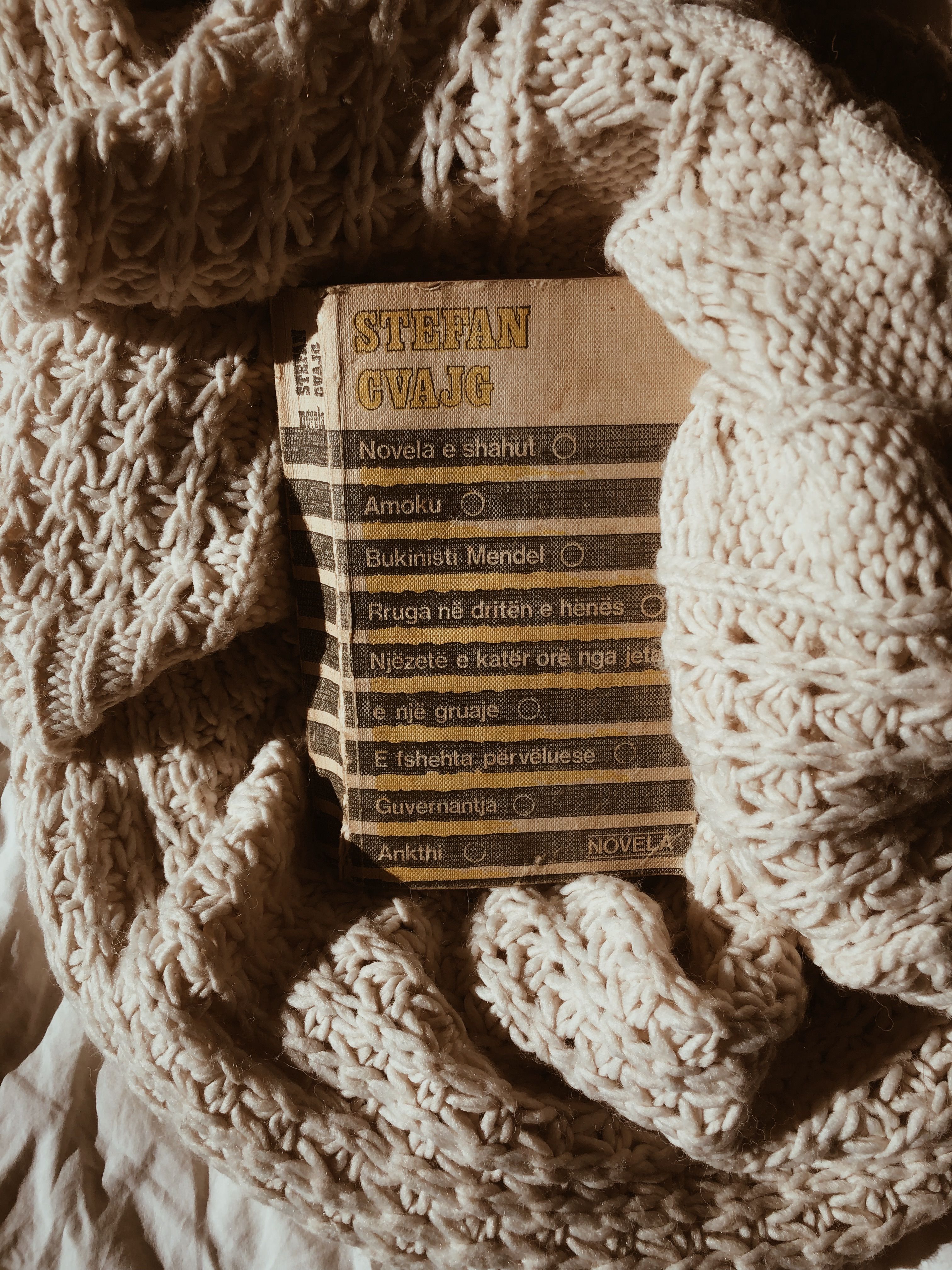Old book tucked in a cozy knitted blanket, evoking vintage relaxation vibes.