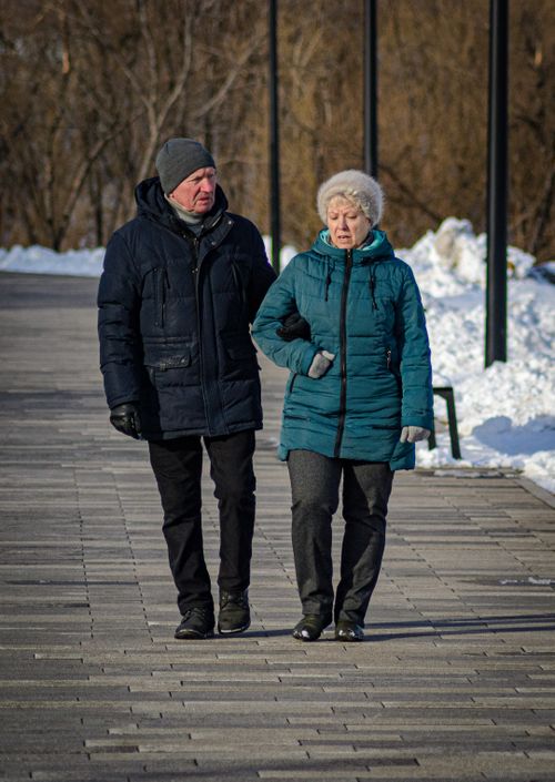 Free A senior couple walks outdoors in winter clothing on a sunny day. Stock Photo