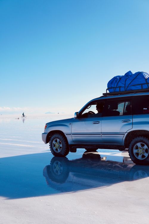 Free A 4x4 vehicle travels across the reflective surface of Bolivia's Salar de Uyuni under a clear sky. Stock Photo