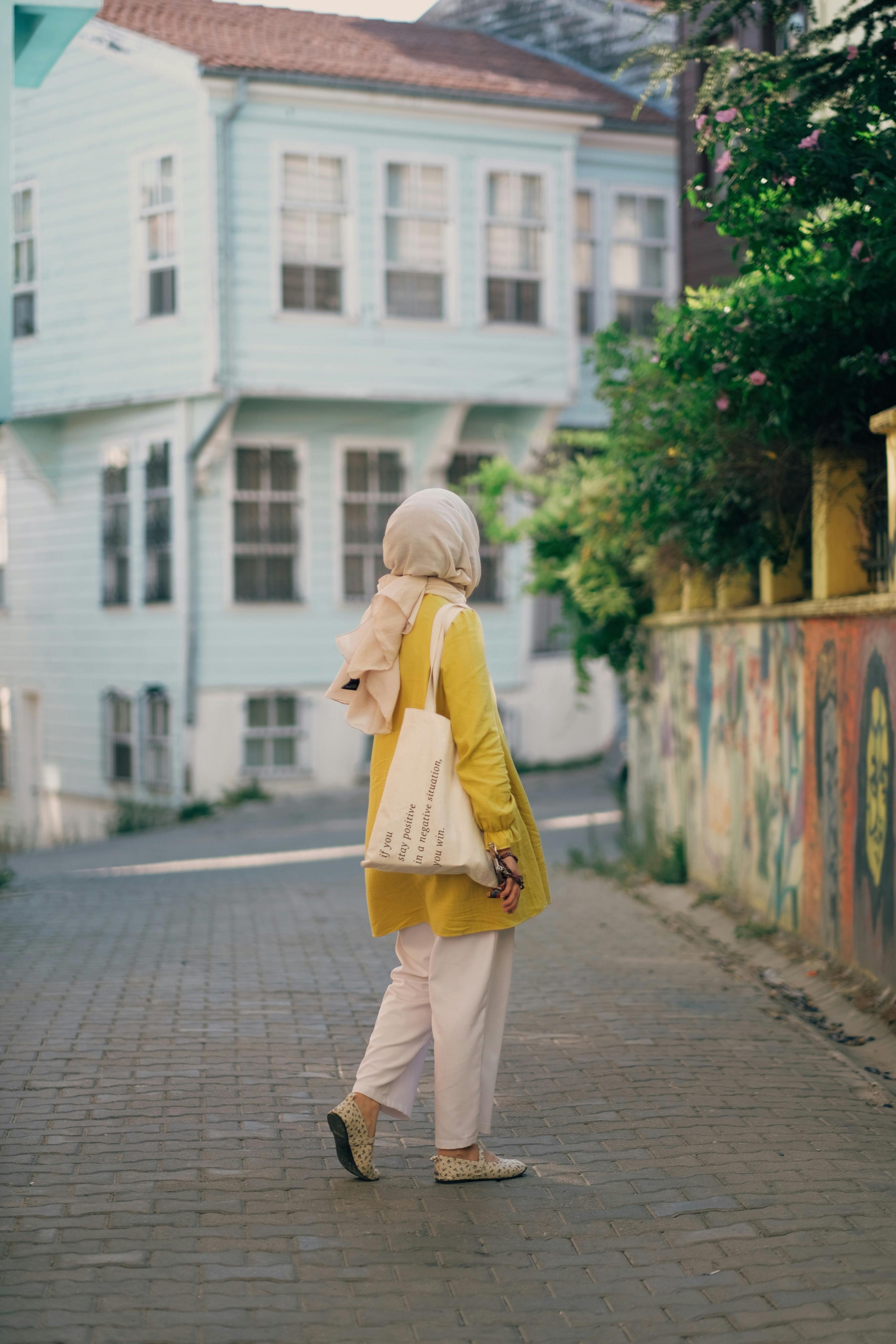 A woman in a headscarf walking on a cobblestone street with colorful houses.