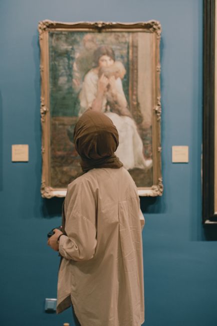 A woman in a museum observes a classic painting on display.