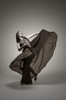 A woman in a flowing dress captures a dynamic dance pose during a black and white studio shoot.