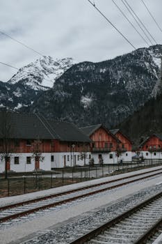 Charming alpine village with colorful homes beneath snowy mountains and railway tracks.