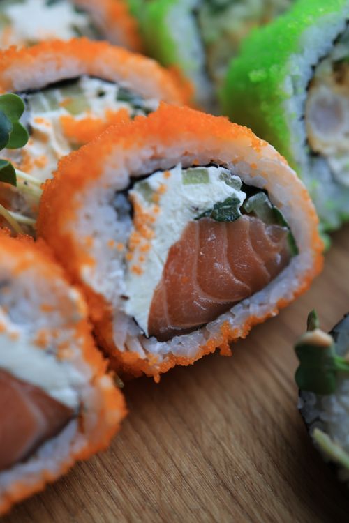 Free Close-up of sushi rolls with fresh salmon, vibrant toppings on a wooden cutting board. Stock Photo