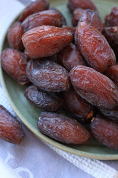 Close-up of a pile of sweet dried dates on a green ceramic plate, perfect for healthy snacking.