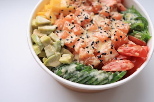 A vibrant salmon poke bowl with fresh avocado, mango, and seaweed, topped with sesame seeds.