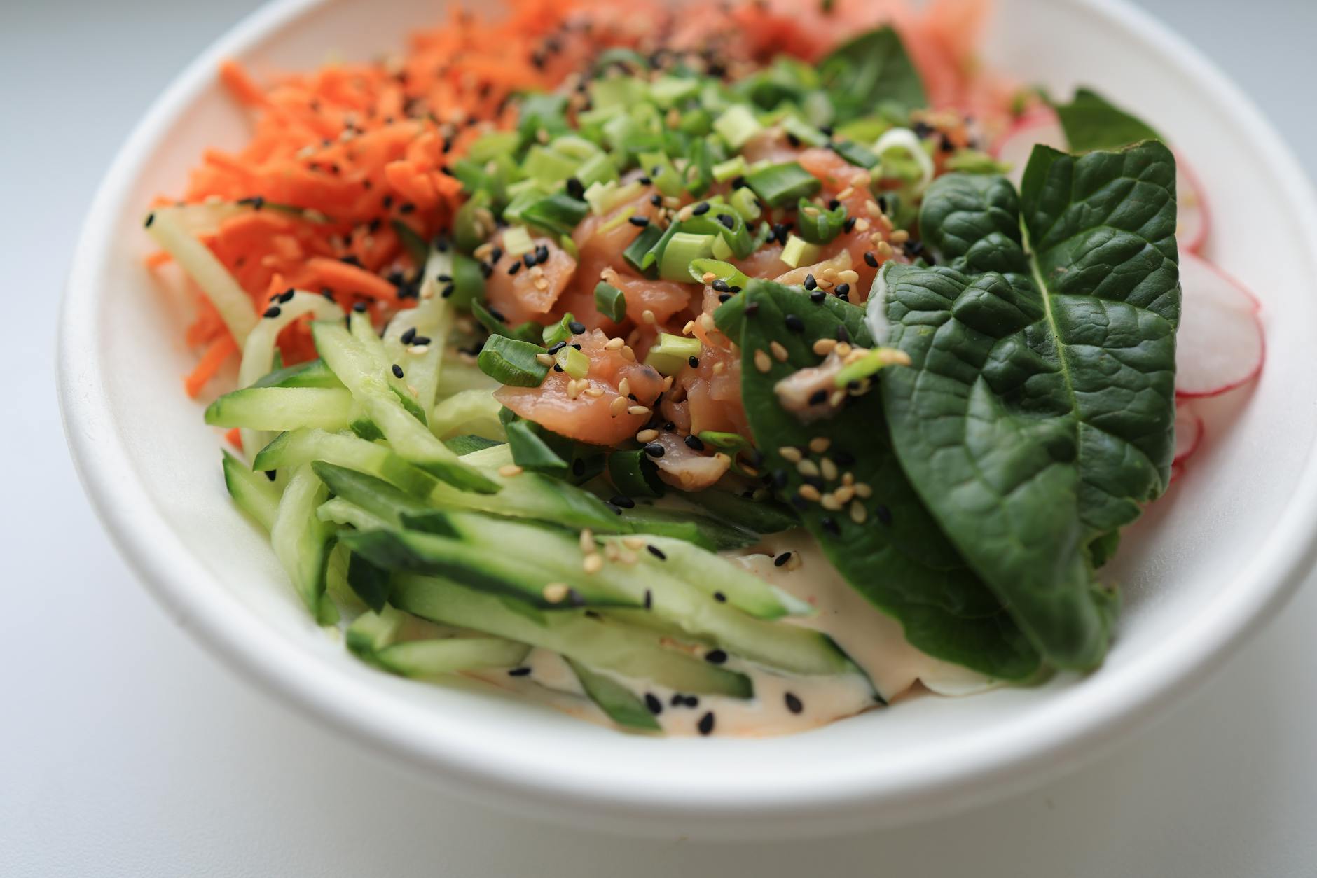 A vibrant salad bowl with salmon, spinach, cucumber, and carrots, perfect for a healthy meal.