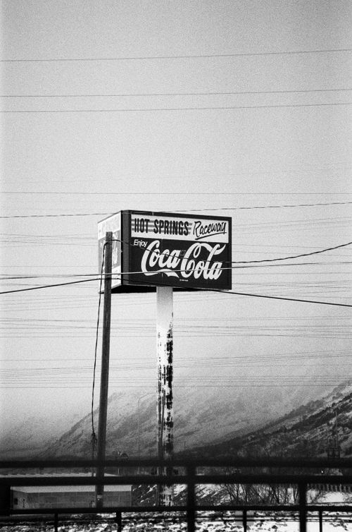 Free Classic Coca-Cola billboard with power lines and mountains in black and white. Stock Photo
