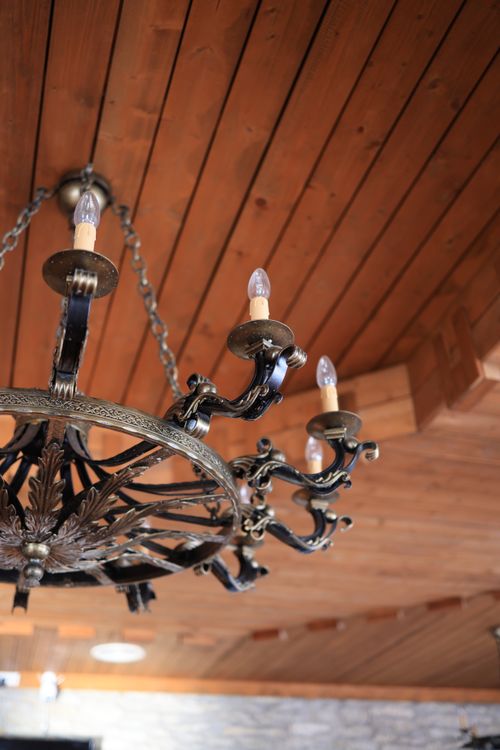 Free An ornate antique chandelier hanging from a rustic wooden ceiling, showcasing intricate metalwork. Stock Photo