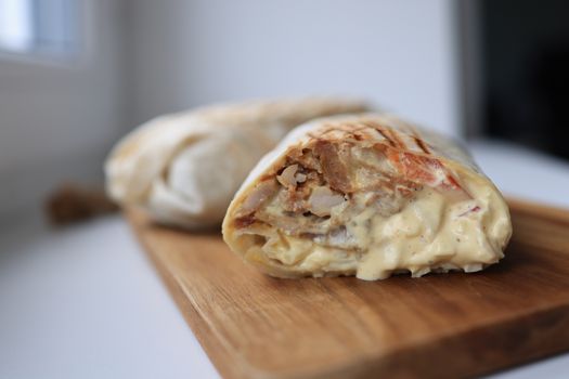Tasty chicken wrap filled with creamy sauce on a wooden cutting board.