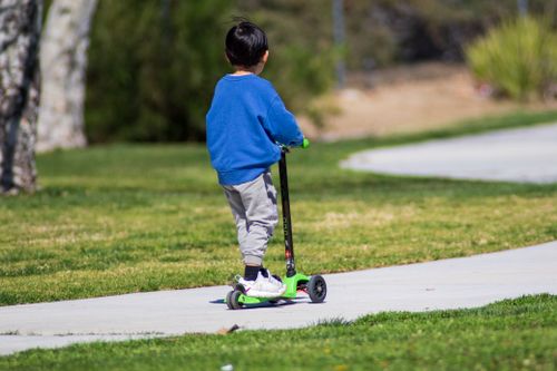 Free A young boy riding a green scooter on a sunny day in the park. Stock Photo