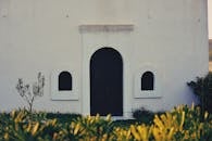 一张照片拍下了极简主义教堂的立面，中央有一扇拱门，周围环绕着植物