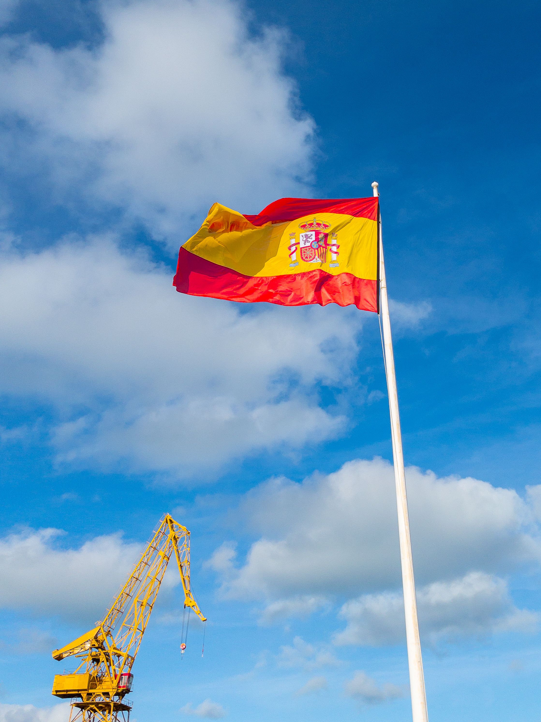 low-angle-shot-of-the-spanish-flag-on-a-flagpole-and-a-crane-in-the