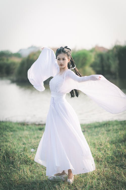 Fashion Model Wearing a Long White Dress Posing on a Lakeshore