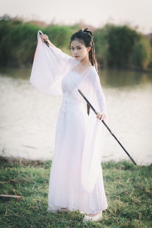 Free Elegant young Asian woman in traditional white dress posing with a sword by the water. Stock Photo