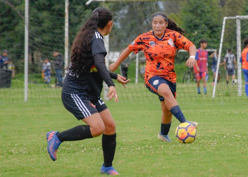 Two women engaged in an outdoor soccer match, showcasing competitive play on a grassy field.