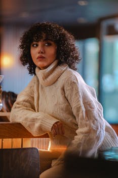 Stylish woman with curly hair in a warm sweater posing indoors.