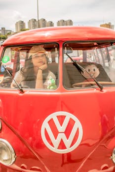 A woman sits in a vintage red Volkswagen in São Paulo, Brazil, against a cityscape backdrop.