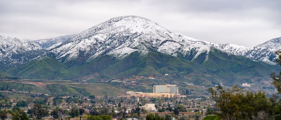 A winter aerial view of snow-capped mountains with San Bernardino cityscape in the foreground, California.