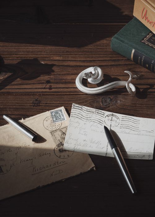 Free Artistic shot of a silver snake pen holder with vintage letters on a wooden table. Stock Photo