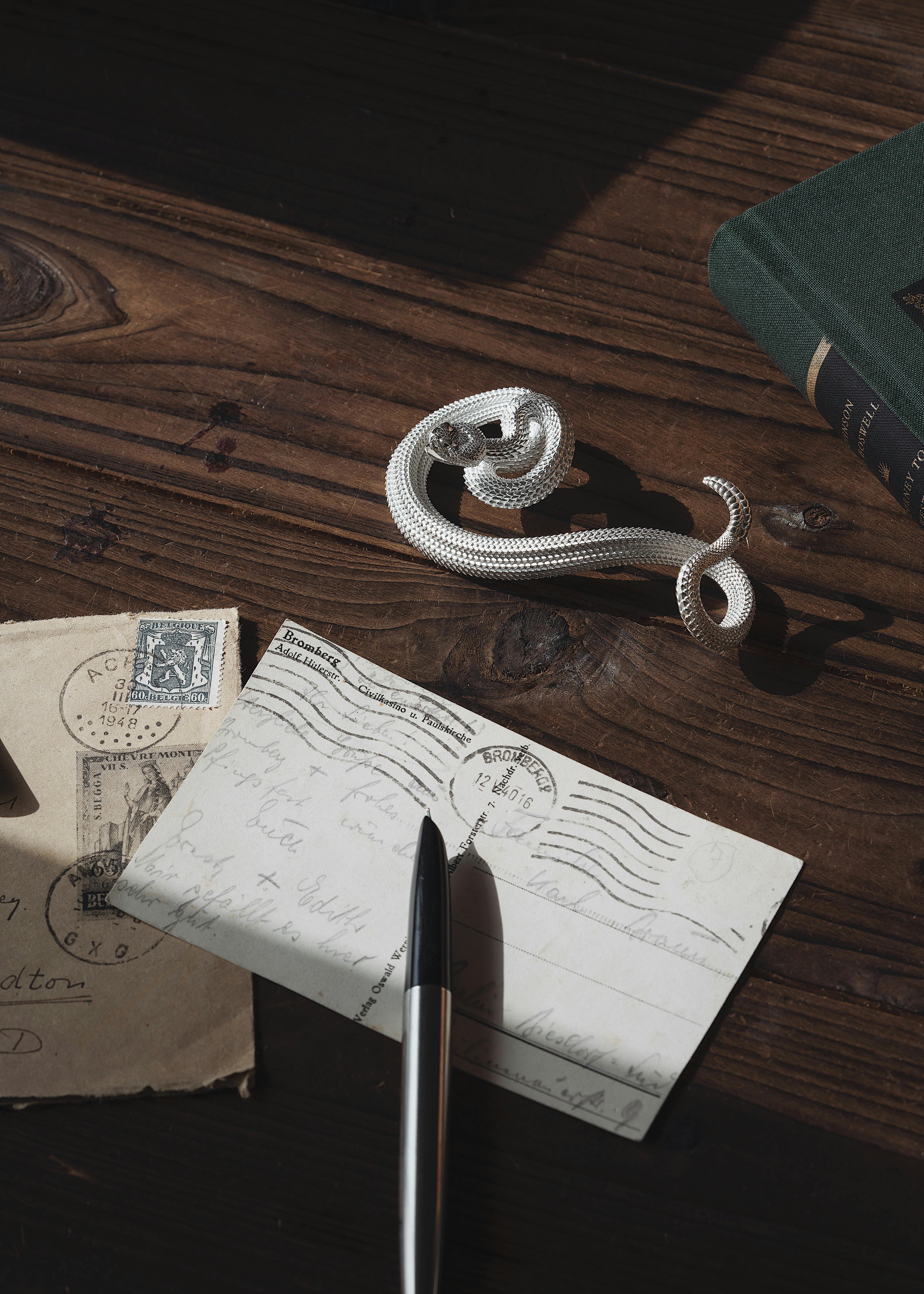 Free Elegant still life featuring a silver snake-shaped pen holder, postcards, and a book on a wooden desk. Stock Photo