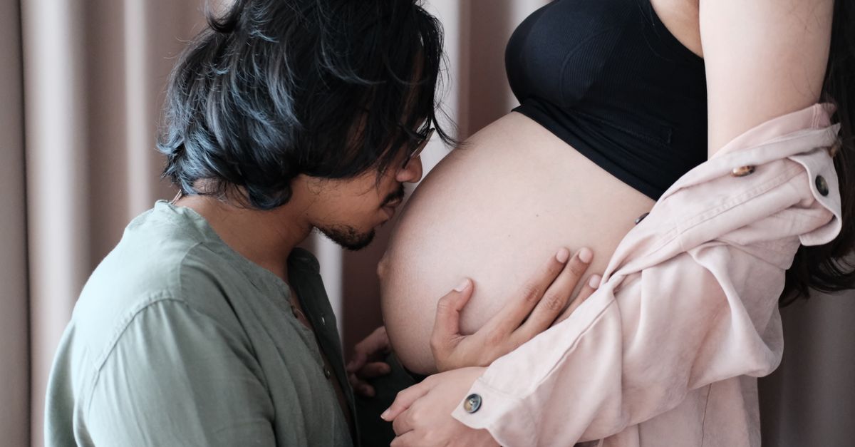 A tender moment of a couple embracing pregnancy, with a man kissing the woman's belly.