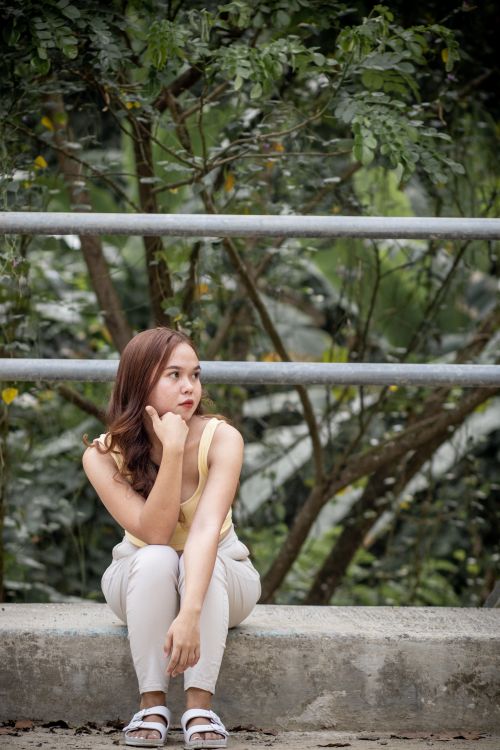 Free Young woman sitting thoughtfully near railings in a natural outdoor setting. Stock Photo