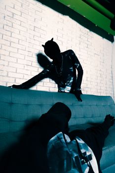 Dramatic silhouette of a person posing on a sofa against a white brick wall.
