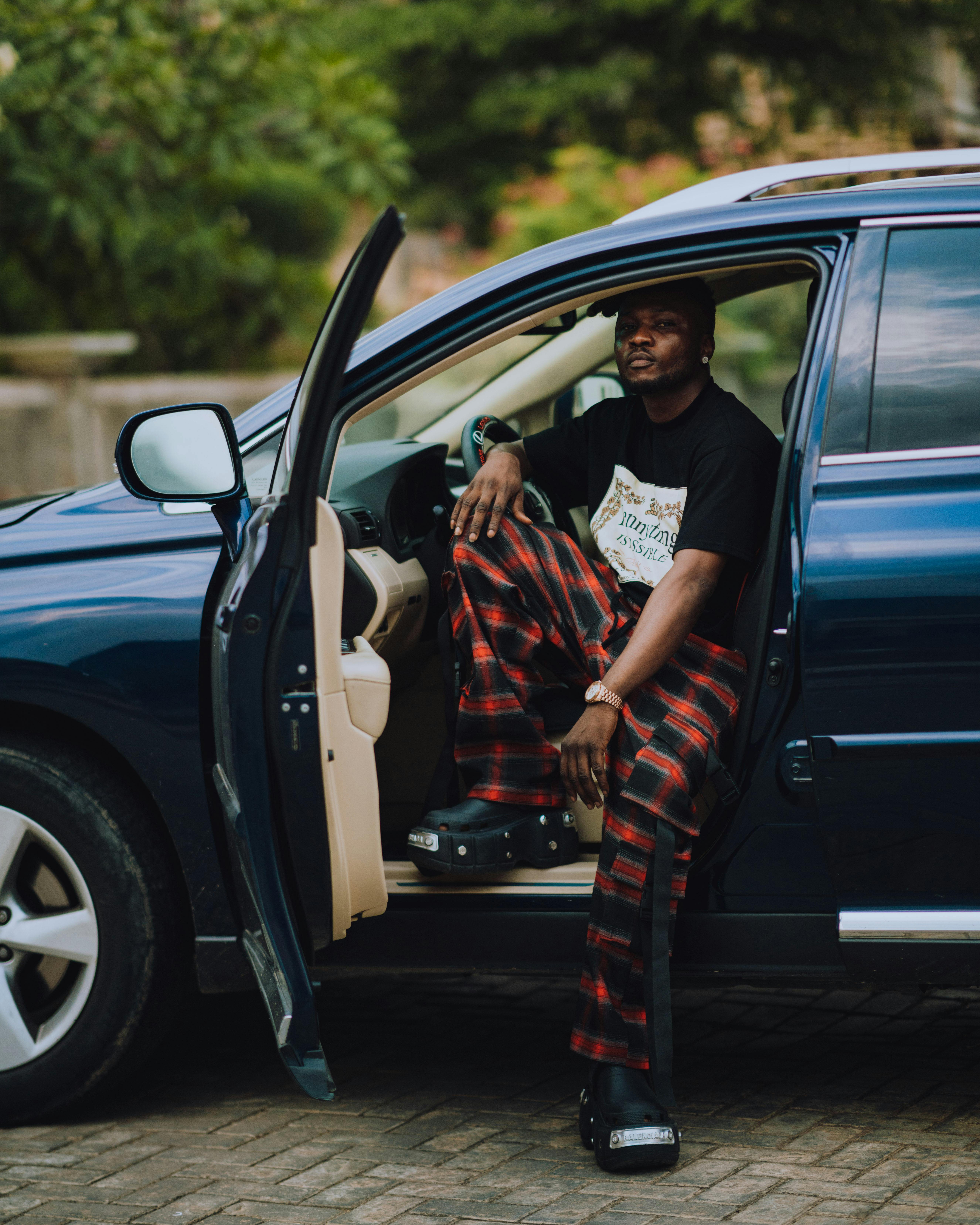 Black man with dreadlocks sitting in a car with the door open, wearing striped pants.
