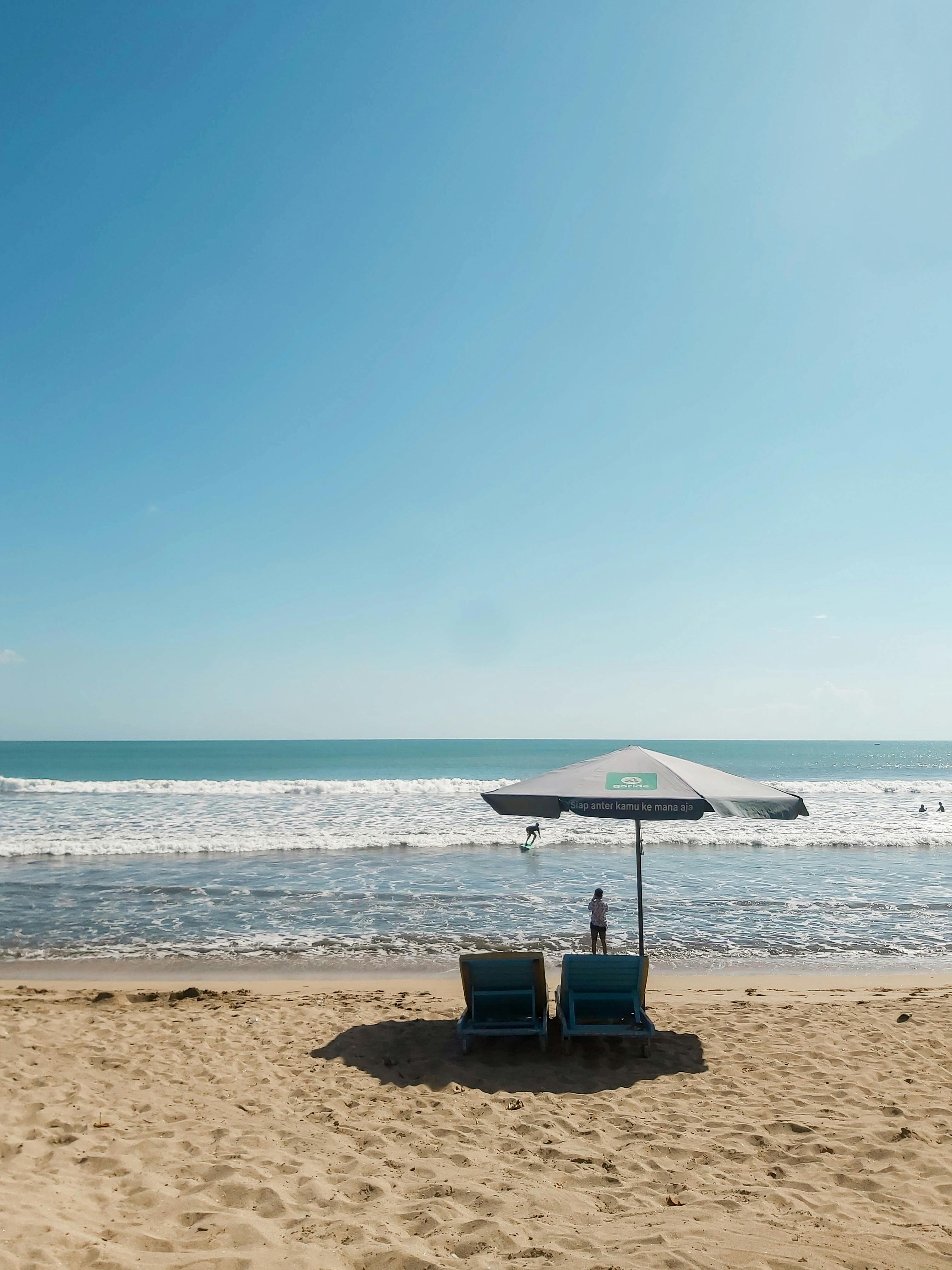 Two deck chairs under an umbrella on Kuta Beach, Bali with a stunning ocean view.