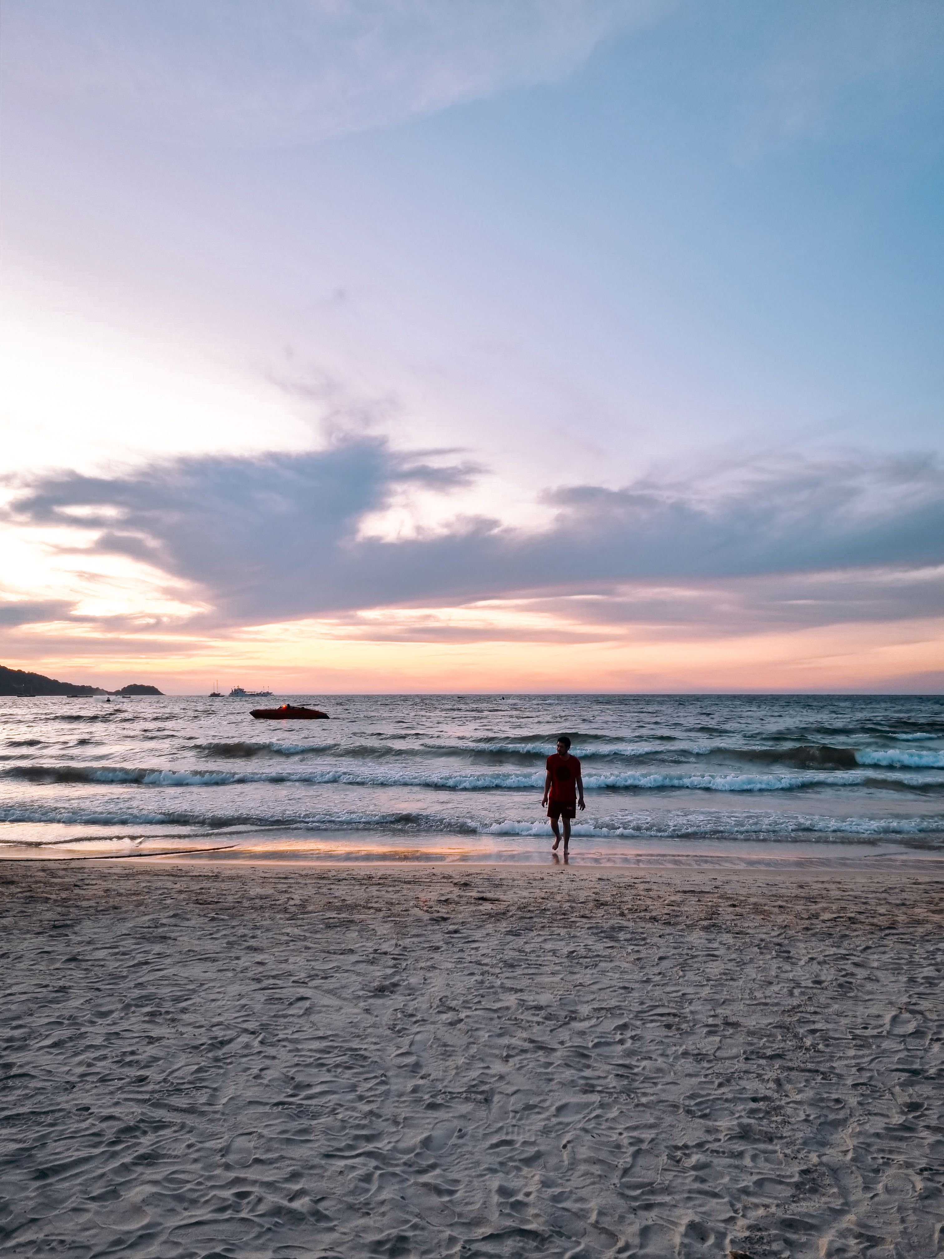 A serene evening scene of a lone figure walking on Patong Beach, Thailand.