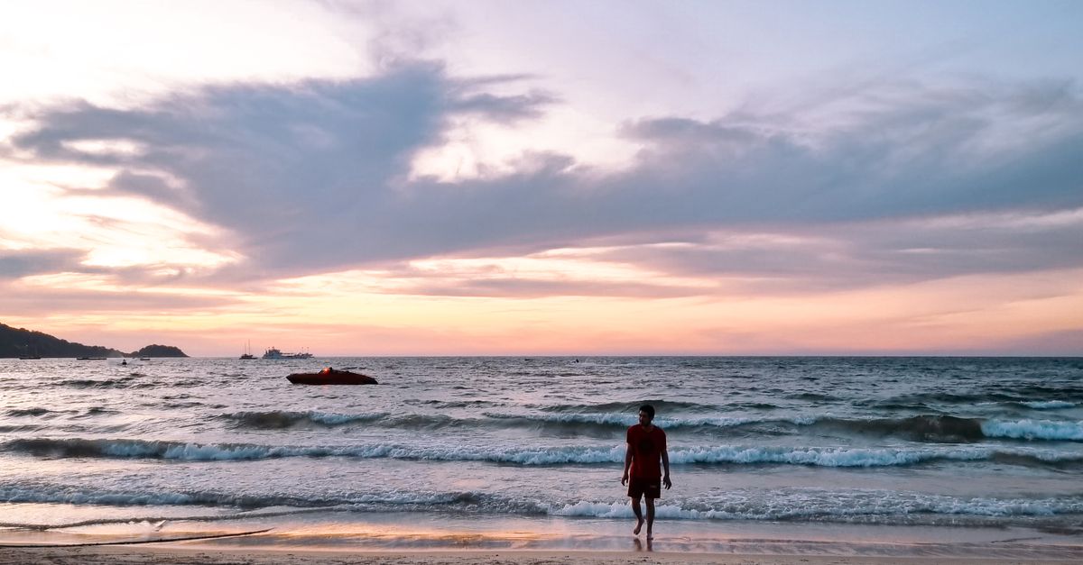 A serene evening scene of a lone figure walking on Patong Beach, Thailand.