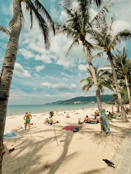 Sunny day at Patong Beach, Phuket, Thailand, featuring palm trees, sand, and relaxing tourists.