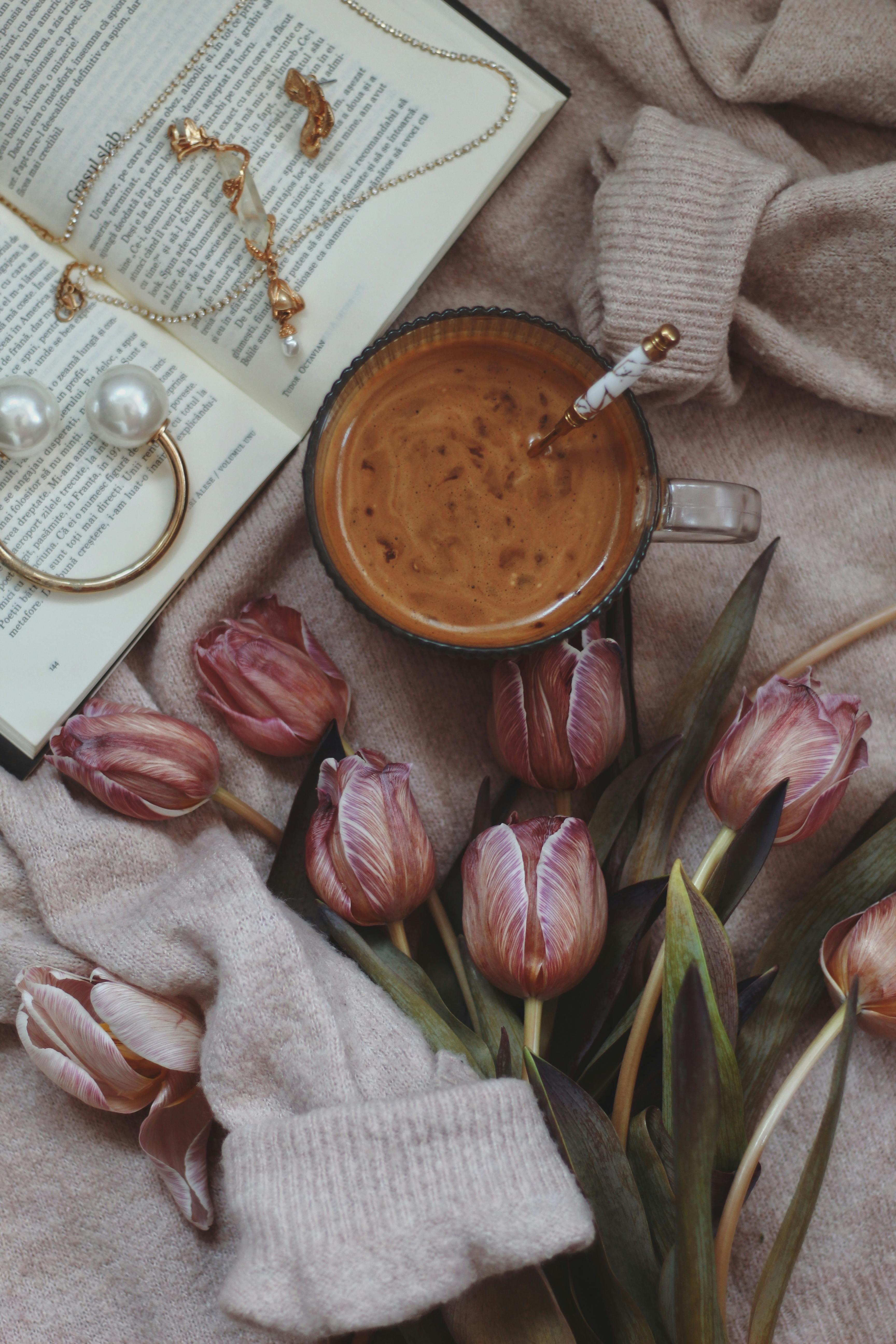 A warm, inviting scene of coffee, purple tulips, an open book, and jewelry in soft lighting.