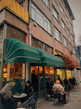 Un café de rue accueillant avec des gens profitant de leur café et de livres sous des auvents verts.