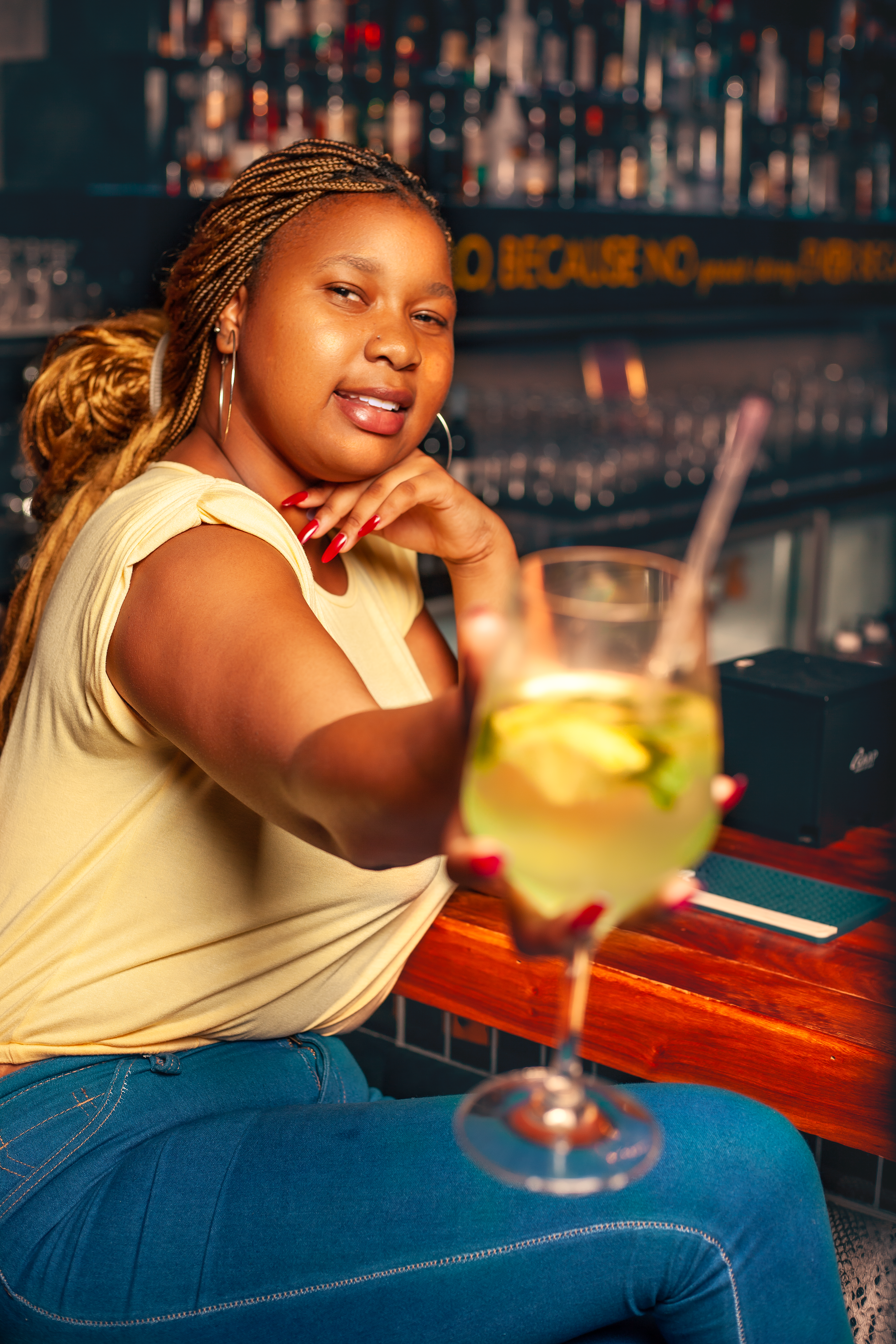 A cheerful woman offering a cocktail while sitting at a bar counter.